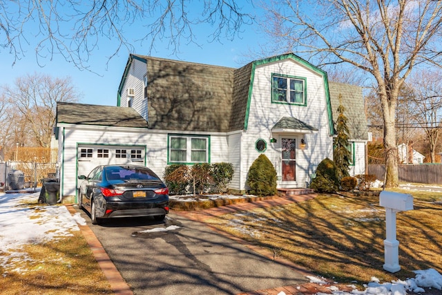 colonial inspired home featuring aphalt driveway, roof with shingles, a gambrel roof, fence, and a garage