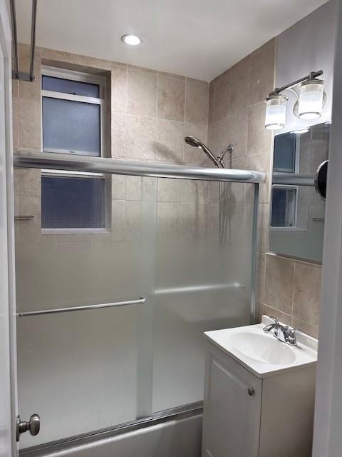 bathroom with tasteful backsplash, enclosed tub / shower combo, vanity, and tile walls