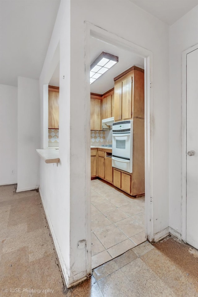 kitchen with white oven, backsplash, and light brown cabinetry