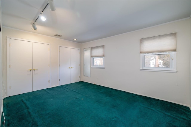 unfurnished bedroom featuring multiple closets, rail lighting, carpet, and crown molding