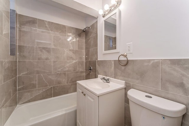 full bathroom featuring tiled shower / bath, vanity, toilet, and tile walls