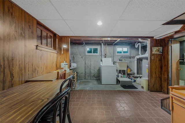 basement with a paneled ceiling, washer and clothes dryer, and wood walls