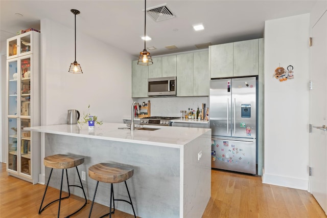 kitchen with a kitchen bar, sink, decorative light fixtures, stainless steel appliances, and light hardwood / wood-style floors