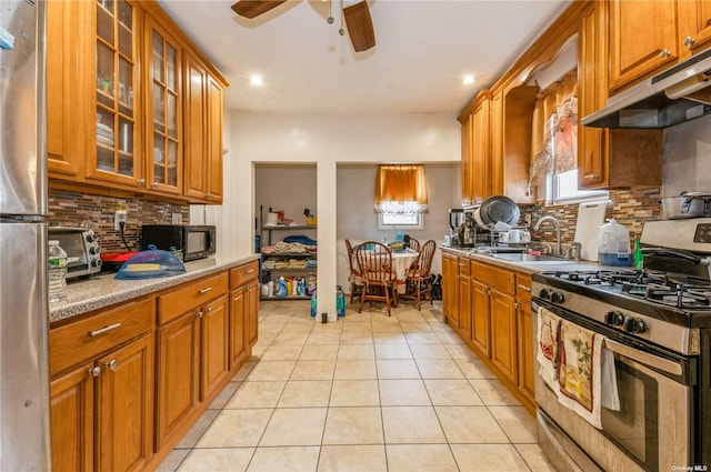 kitchen featuring light tile patterned flooring, sink, ceiling fan, stainless steel appliances, and light stone countertops