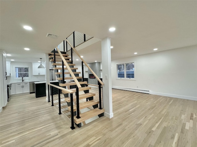 staircase featuring a baseboard radiator, sink, and hardwood / wood-style floors