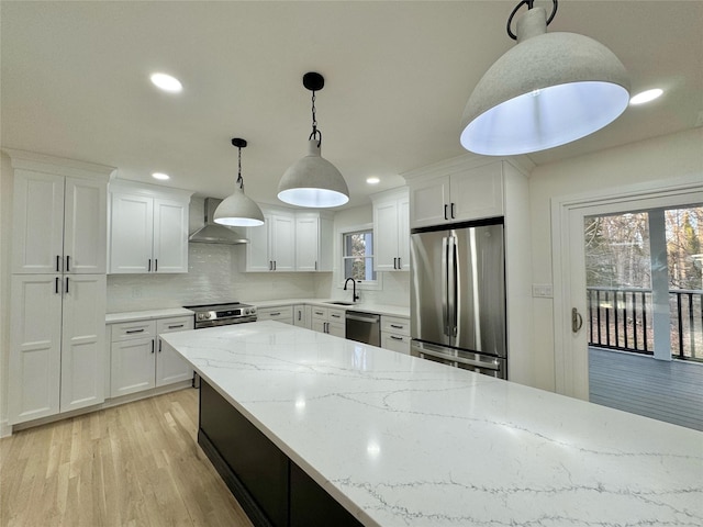 kitchen featuring white cabinetry, hanging light fixtures, stainless steel appliances, and wall chimney exhaust hood