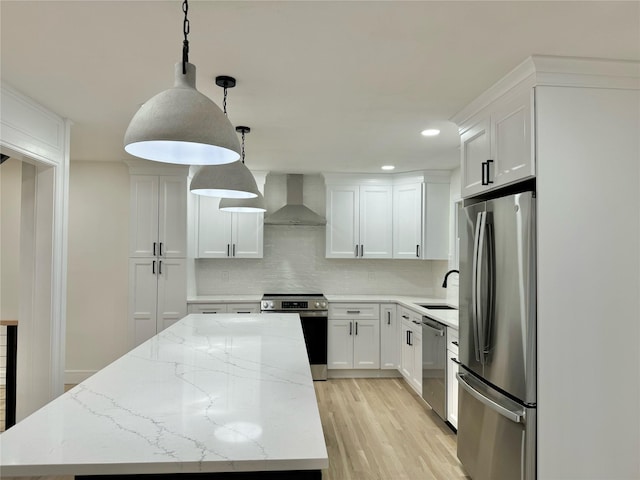 kitchen featuring wall chimney exhaust hood, appliances with stainless steel finishes, hanging light fixtures, and white cabinets