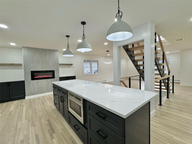 kitchen with stainless steel microwave, a fireplace, hanging light fixtures, a center island, and light hardwood / wood-style floors