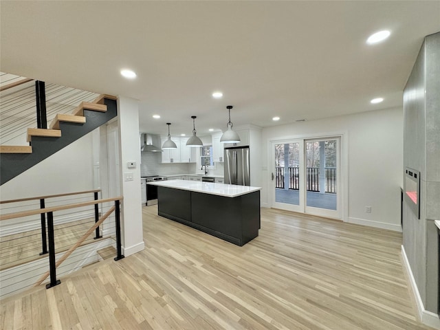 kitchen featuring pendant lighting, wall chimney range hood, stainless steel appliances, white cabinets, and a kitchen island