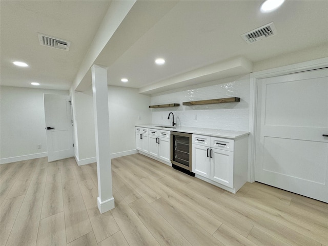 bar featuring sink, white cabinetry, backsplash, light hardwood / wood-style floors, and beverage cooler