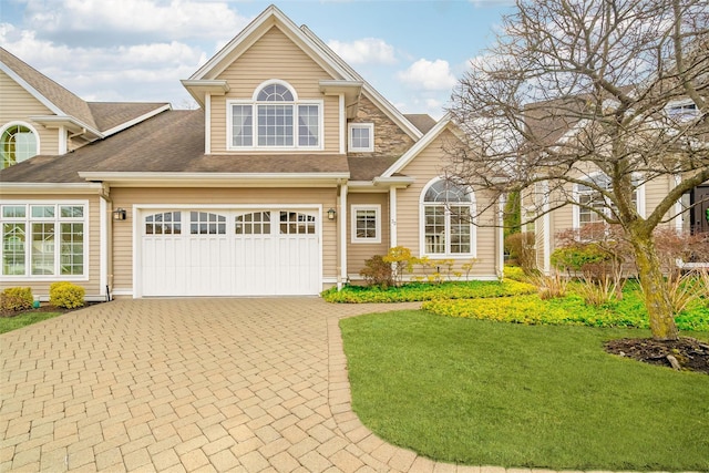 view of front facade featuring a garage, stone siding, roof with shingles, decorative driveway, and a front lawn