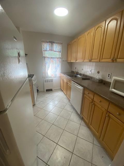 kitchen featuring radiator heating unit, sink, backsplash, light tile patterned floors, and white appliances