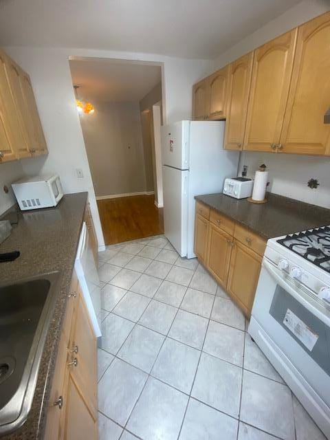 kitchen with light tile patterned flooring, sink, light brown cabinets, and white appliances