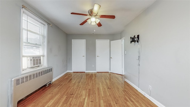 empty room featuring cooling unit, ceiling fan, radiator, and light hardwood / wood-style flooring