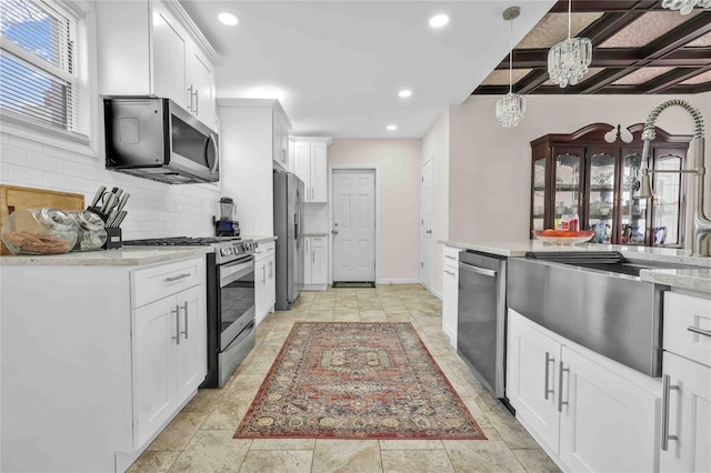 kitchen featuring decorative backsplash, stainless steel appliances, hanging light fixtures, and white cabinets