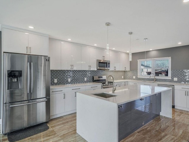 kitchen with decorative light fixtures, sink, white cabinets, stainless steel appliances, and a center island with sink