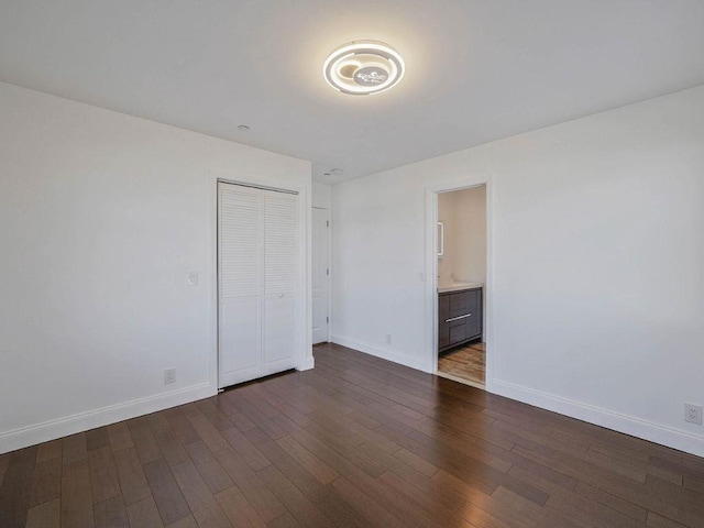 unfurnished bedroom with dark wood-type flooring, a closet, and ensuite bathroom