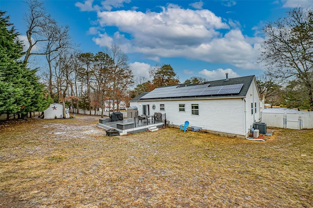 back of house featuring a lawn, a shed, a wooden deck, solar panels, and central air condition unit