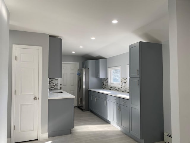 kitchen with gray cabinets, a baseboard radiator, sink, and stainless steel refrigerator