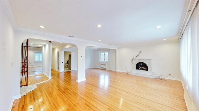 unfurnished living room featuring a premium fireplace, crown molding, and light wood-type flooring