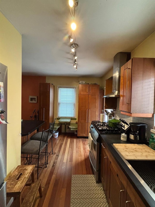 kitchen featuring hardwood / wood-style flooring, wall chimney range hood, tasteful backsplash, and stainless steel gas stove