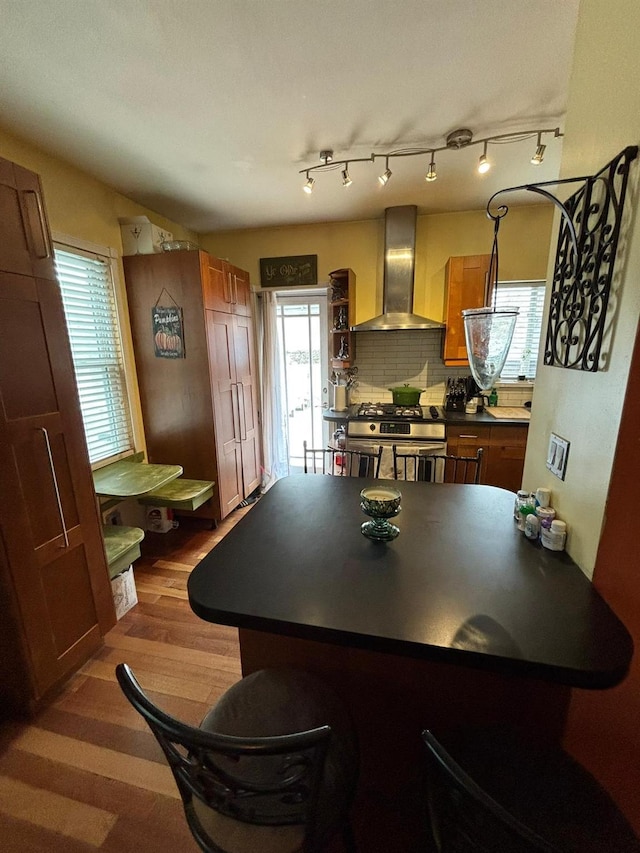 kitchen featuring wall chimney range hood, stainless steel gas range, a breakfast bar, hardwood / wood-style floors, and tasteful backsplash