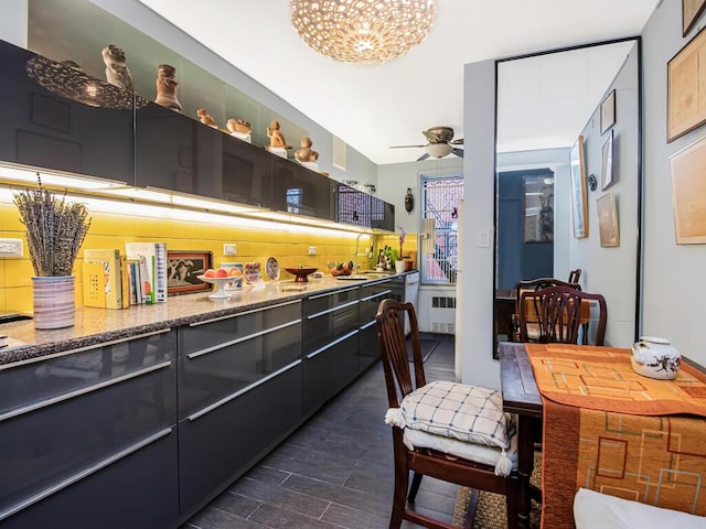 kitchen with sink, tasteful backsplash, light stone counters, radiator heating unit, and ceiling fan