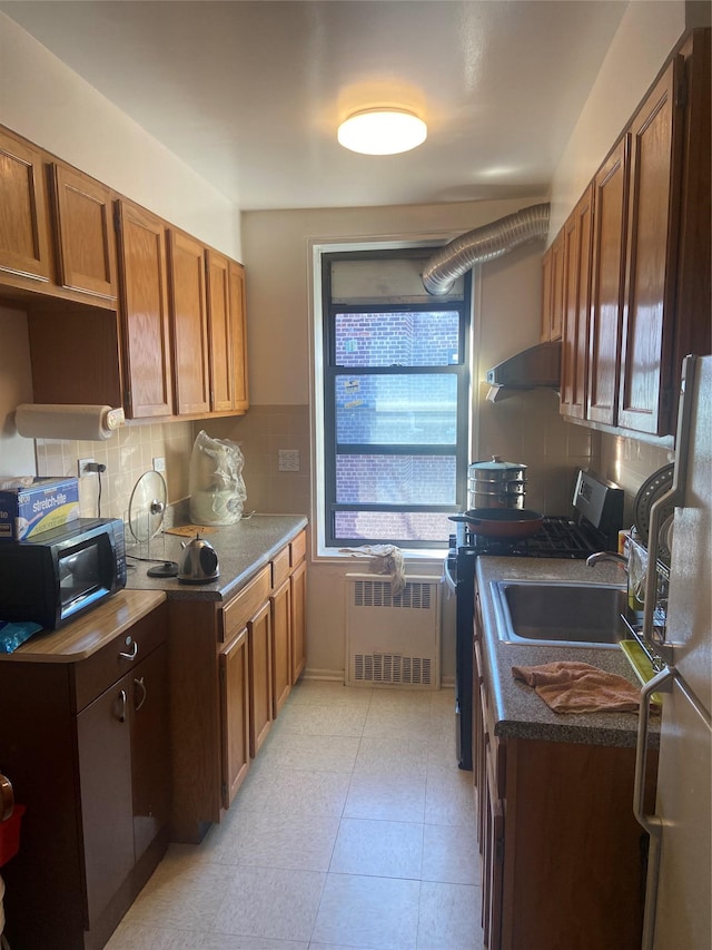 kitchen with white fridge, radiator heating unit, decorative backsplash, and stainless steel gas stove