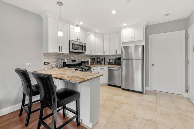 kitchen with appliances with stainless steel finishes, white cabinetry, light stone counters, decorative light fixtures, and kitchen peninsula