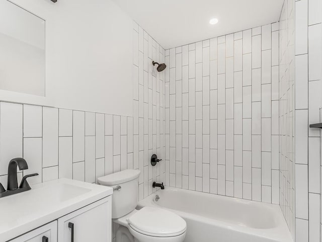 full bathroom with tile walls, vanity, tiled shower / bath combo, and toilet