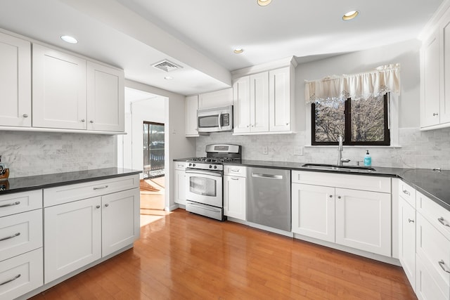 kitchen featuring sink, appliances with stainless steel finishes, tasteful backsplash, white cabinets, and light wood-type flooring