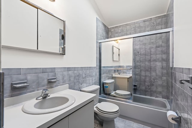 full bathroom featuring toilet, vanity, bath / shower combo with glass door, and tile walls