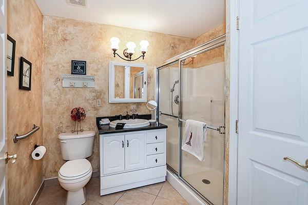 bathroom featuring walk in shower, vanity, toilet, and tile patterned flooring