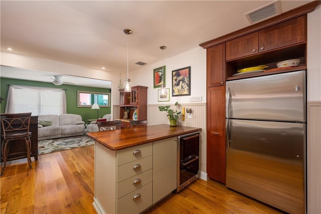 kitchen featuring stainless steel refrigerator, decorative light fixtures, kitchen peninsula, and light wood-type flooring