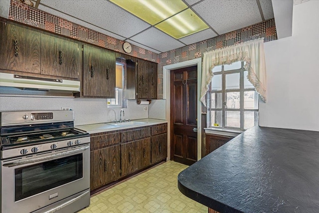 kitchen with sink, stainless steel stove, dark brown cabinets, and a drop ceiling