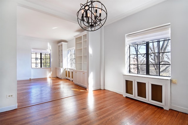 unfurnished dining area with a notable chandelier, ornamental molding, and light wood-type flooring