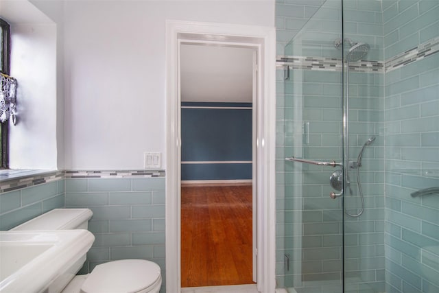 bathroom featuring a shower with door, tile walls, and toilet