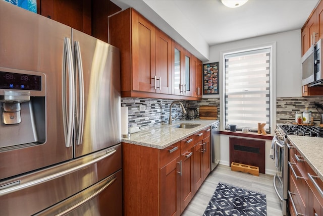 kitchen featuring appliances with stainless steel finishes, light stone countertops, sink, and backsplash