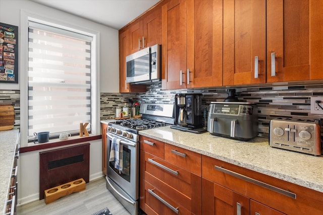 kitchen with light stone counters, appliances with stainless steel finishes, tasteful backsplash, and light wood-type flooring