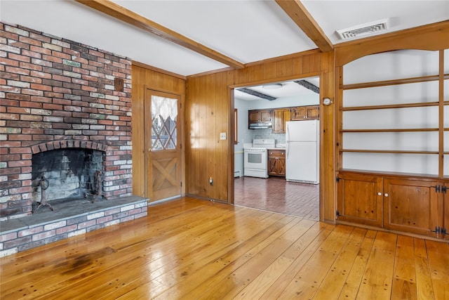 unfurnished living room with beamed ceiling, a brick fireplace, wooden walls, and light hardwood / wood-style flooring