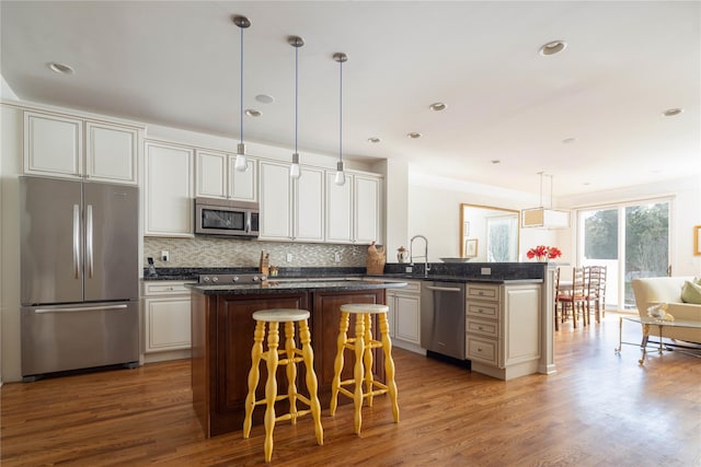 kitchen featuring wood-type flooring, appliances with stainless steel finishes, a center island, and backsplash