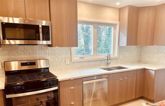 kitchen with sink, decorative backsplash, stainless steel appliances, and light stone countertops