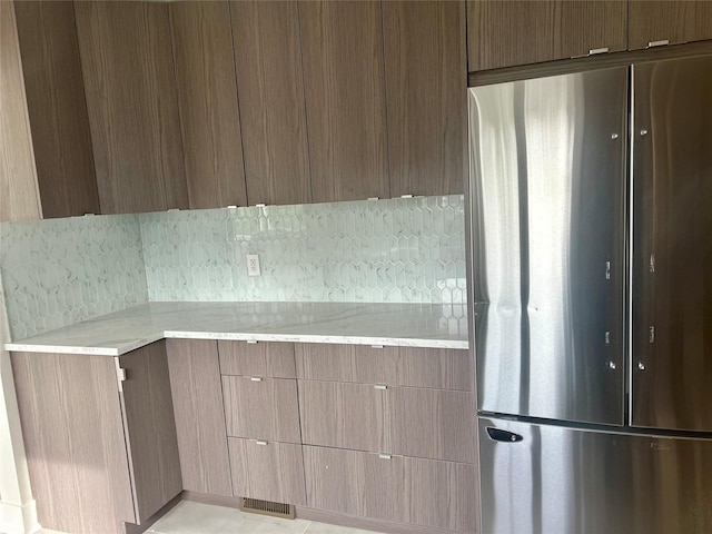 kitchen featuring tasteful backsplash, stainless steel fridge, and light stone counters