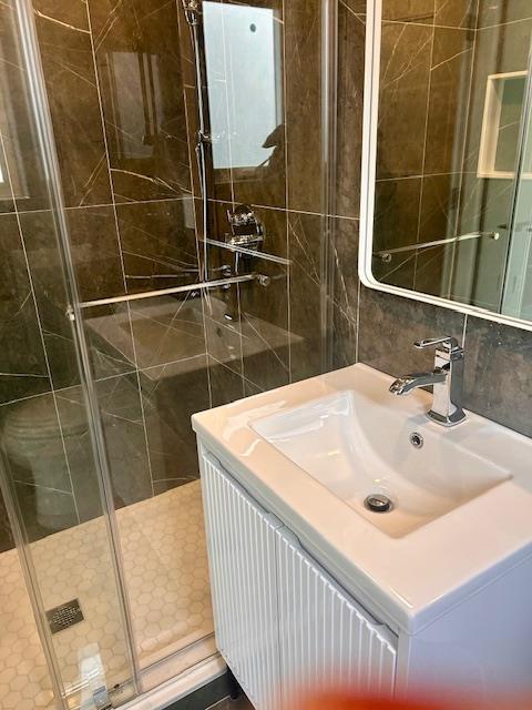 bathroom with vanity, a shower with door, tile walls, and backsplash