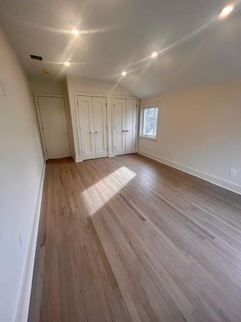 unfurnished bedroom with vaulted ceiling, light hardwood / wood-style floors, and multiple closets