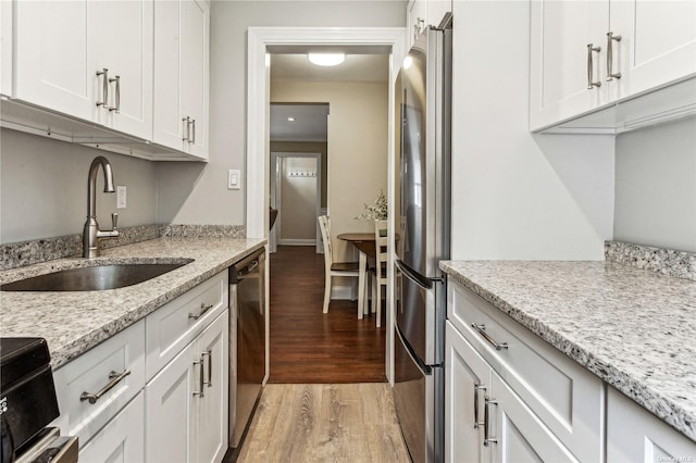 kitchen with sink, white cabinets, light stone counters, light hardwood / wood-style floors, and stainless steel appliances