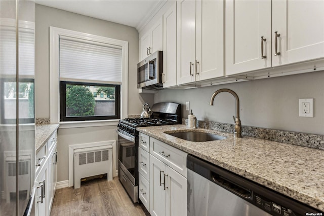 kitchen featuring white cabinetry, light wood-type flooring, radiator, stainless steel appliances, and light stone countertops