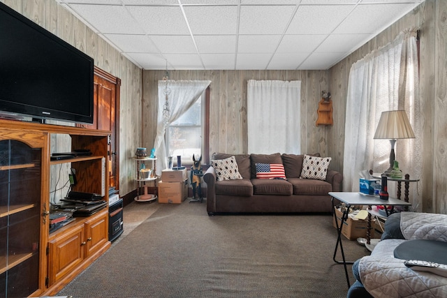 carpeted living room with a drop ceiling, wooden walls, and a healthy amount of sunlight