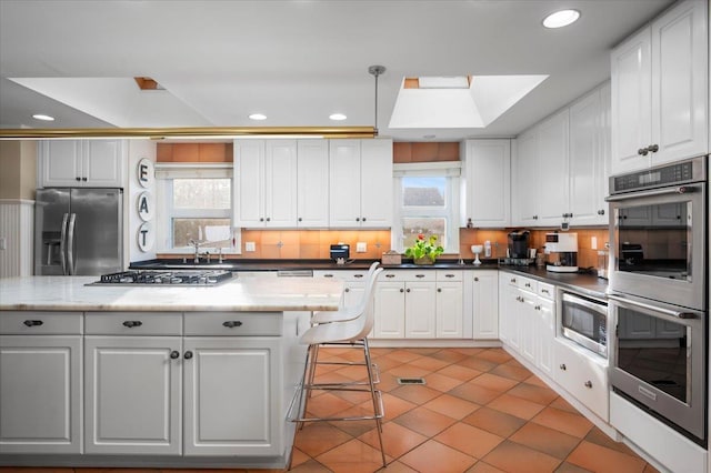 kitchen with plenty of natural light, stainless steel appliances, decorative light fixtures, and white cabinets