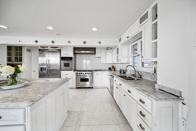 kitchen with sink, high end appliances, light stone counters, white cabinets, and wall chimney exhaust hood